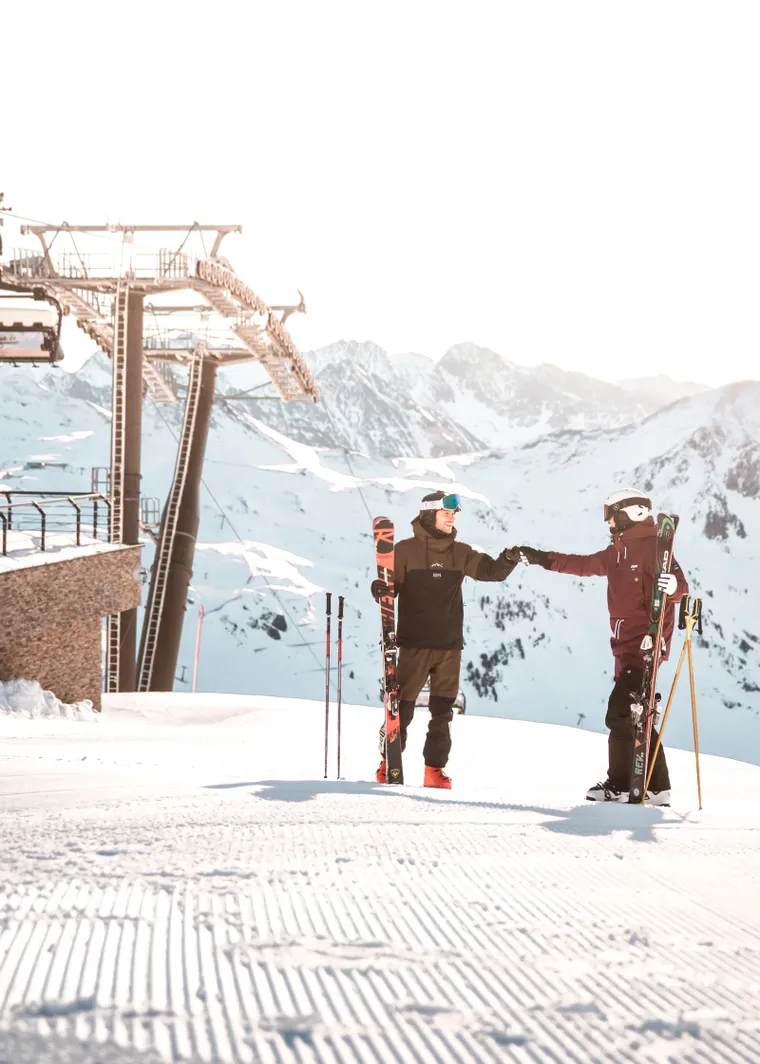Two skiers fist bumping near ski lift station in the snow-covered Alps